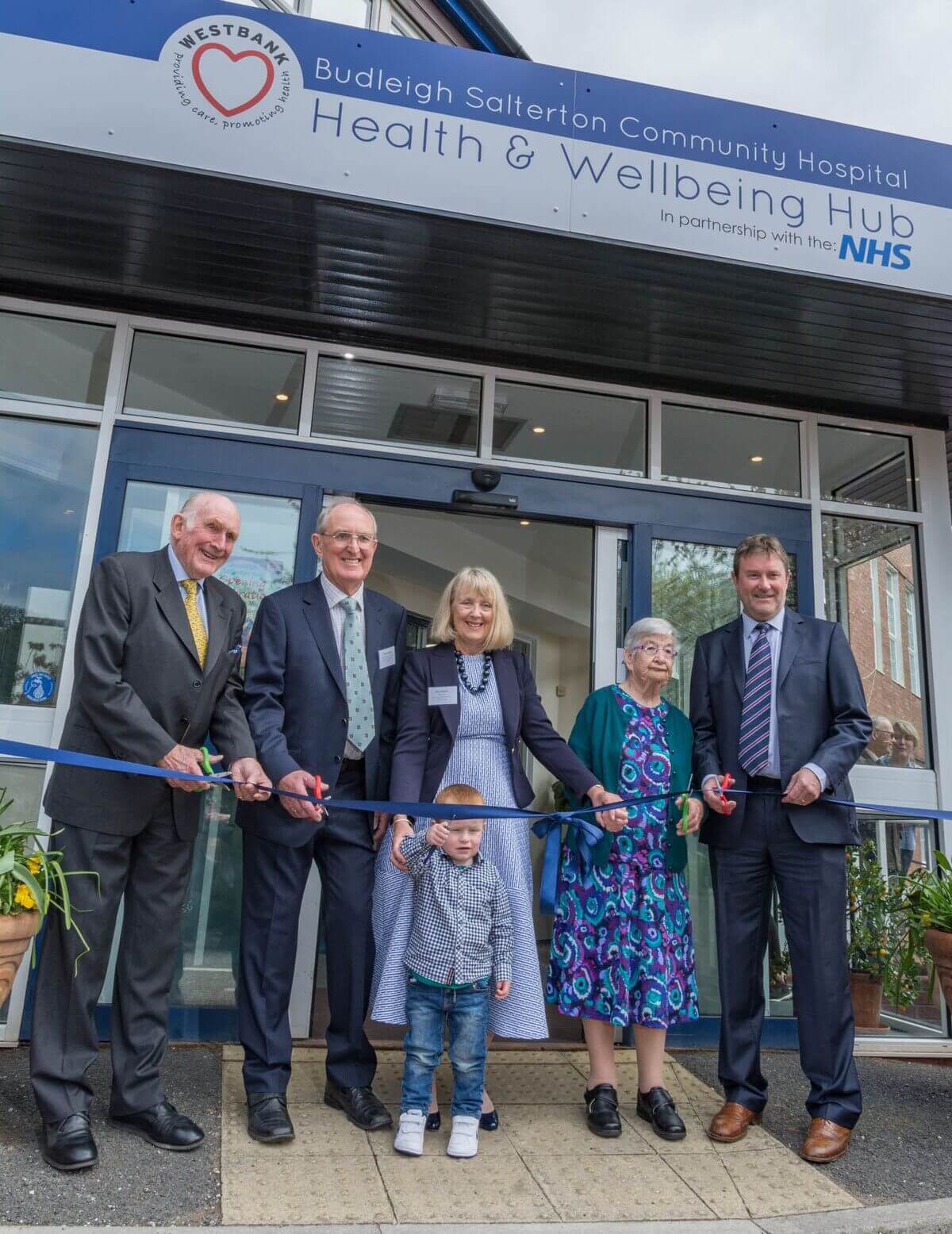 A group of people is holding a ribbon at the opening celebration of Budleigh Hub in Devon