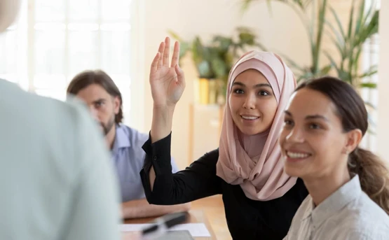 a group of people are watching someone present and a young woman puts her hand in the air