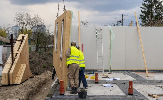 two construction workers in high vis lower a house frame into position