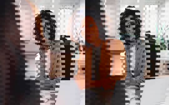 a woman sat at a laptop listens to someone in front of her 