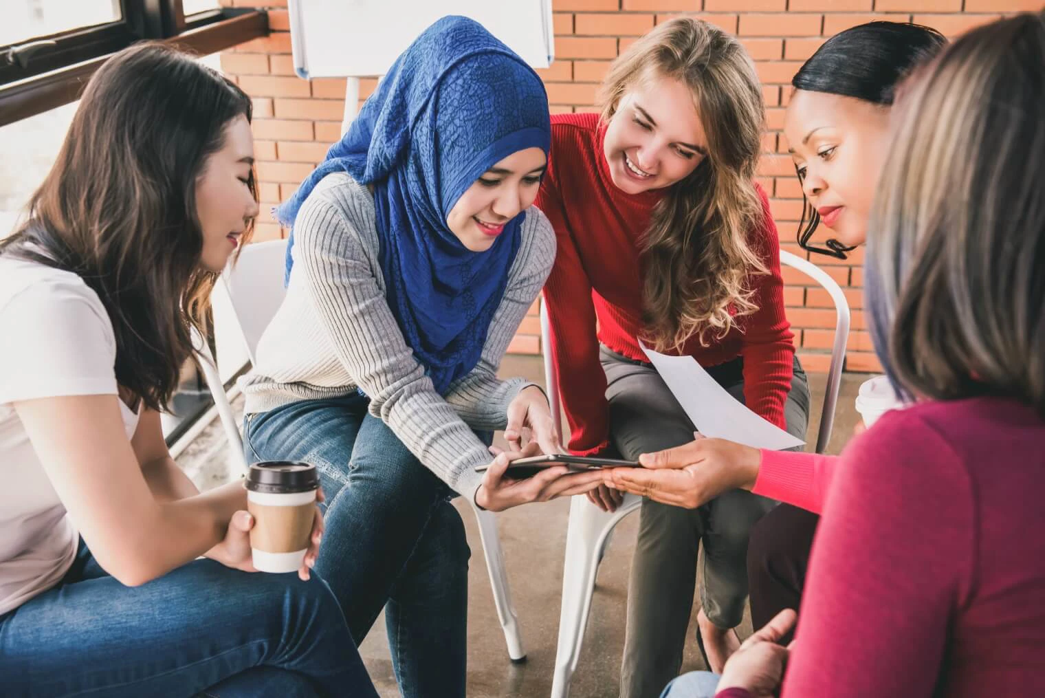 young women of different ethnicity crowd round a tablet smiling 