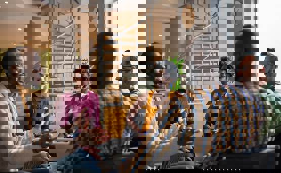 five people in a modern office talk sat in a circle with laptops