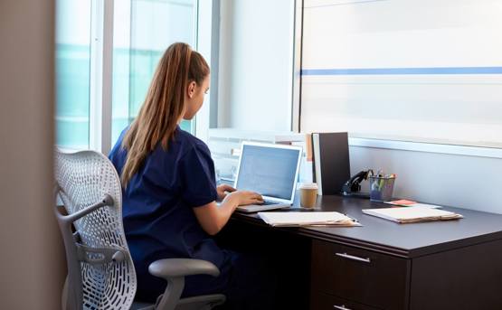 a health care worker sitting at a desk on a laptop 