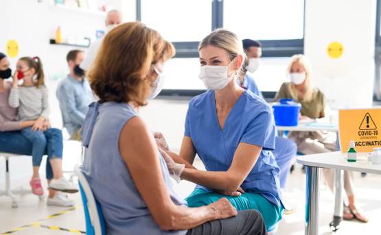 Woman with face mask getting vaccinated by female nurse