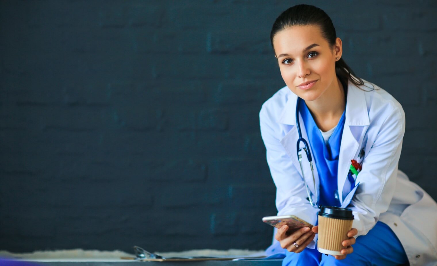 Female Doctor holding coffee cup and a smart phone 