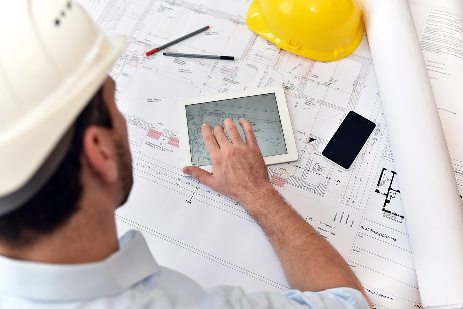 Stock image of man wearing a hard hat looking at building drawings with ipad