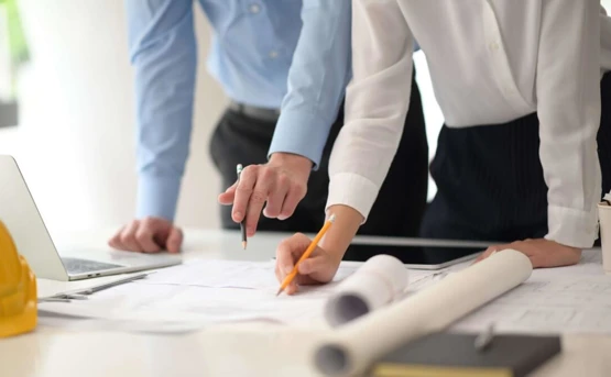Stock image of man and a woman looking a building plans on a desk
