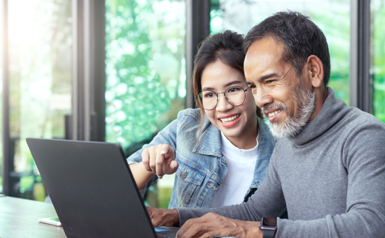 Stock image of Young Woman Teaching Older Man To Use Laptop