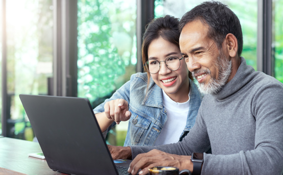 Stock image of Young Woman Teaching Older Man To Use Laptop