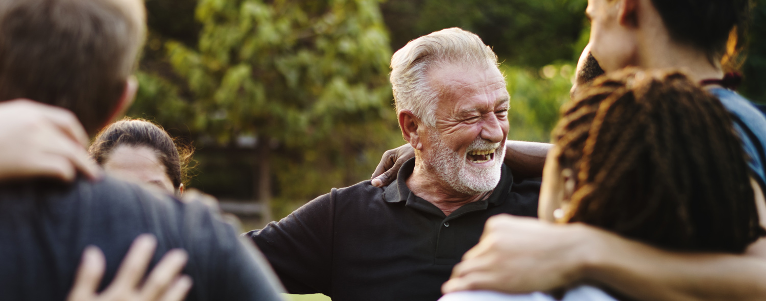 Stock image of a group Of People hugging With Focus On Older Man Laughing