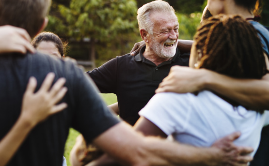Stock image of a group Of People hugging With Focus On Older Man Laughing