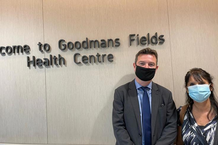 Two NHSPS colleagues standing in front of signage that says 'Welcome to Goodmans Fields Health Centre'