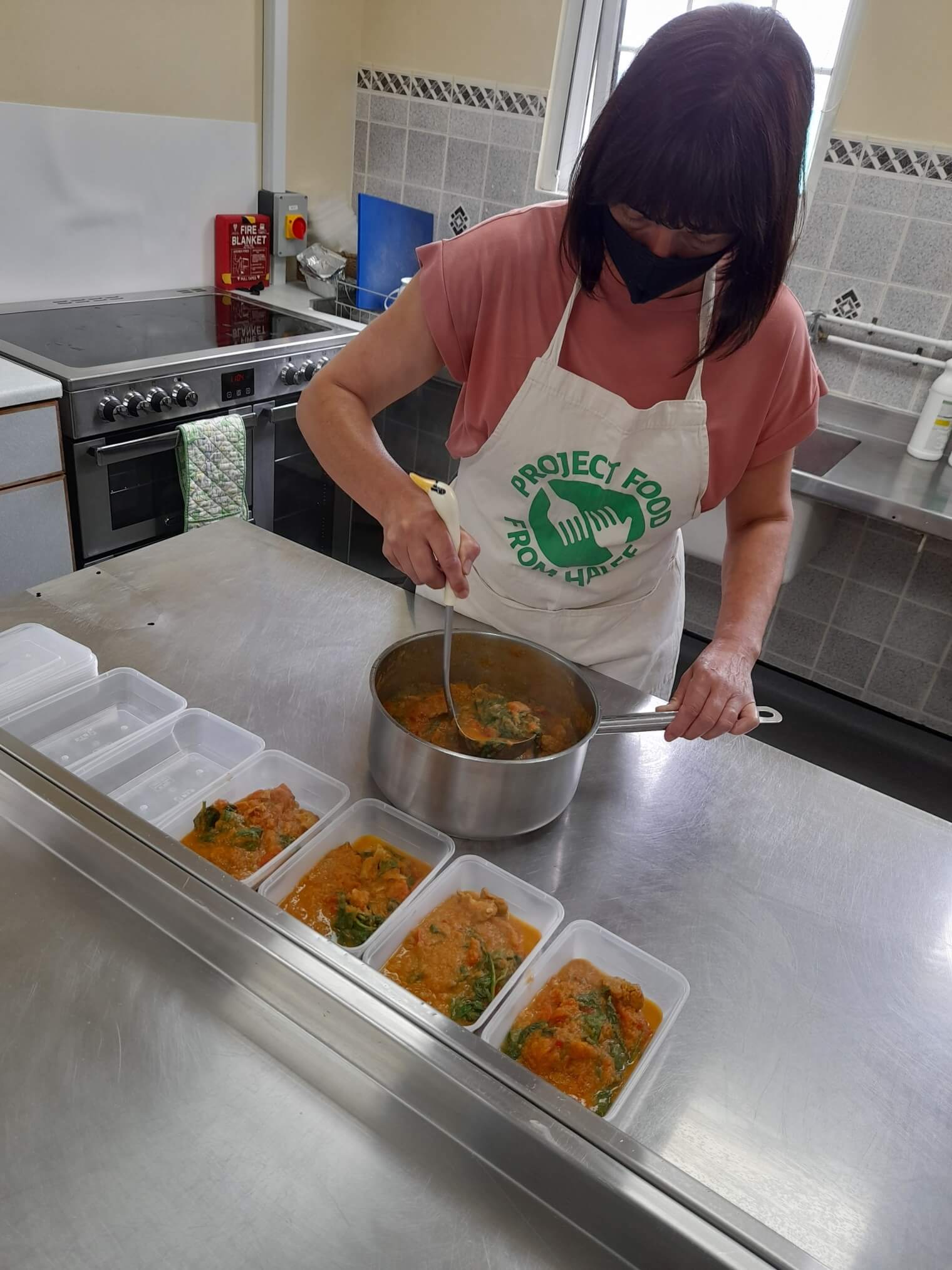 Woman with a Project Food apron on, making a stew and filling Tupperware 