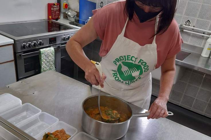 Woman with a Project Food apron on, making a stew and filling Tupperware 