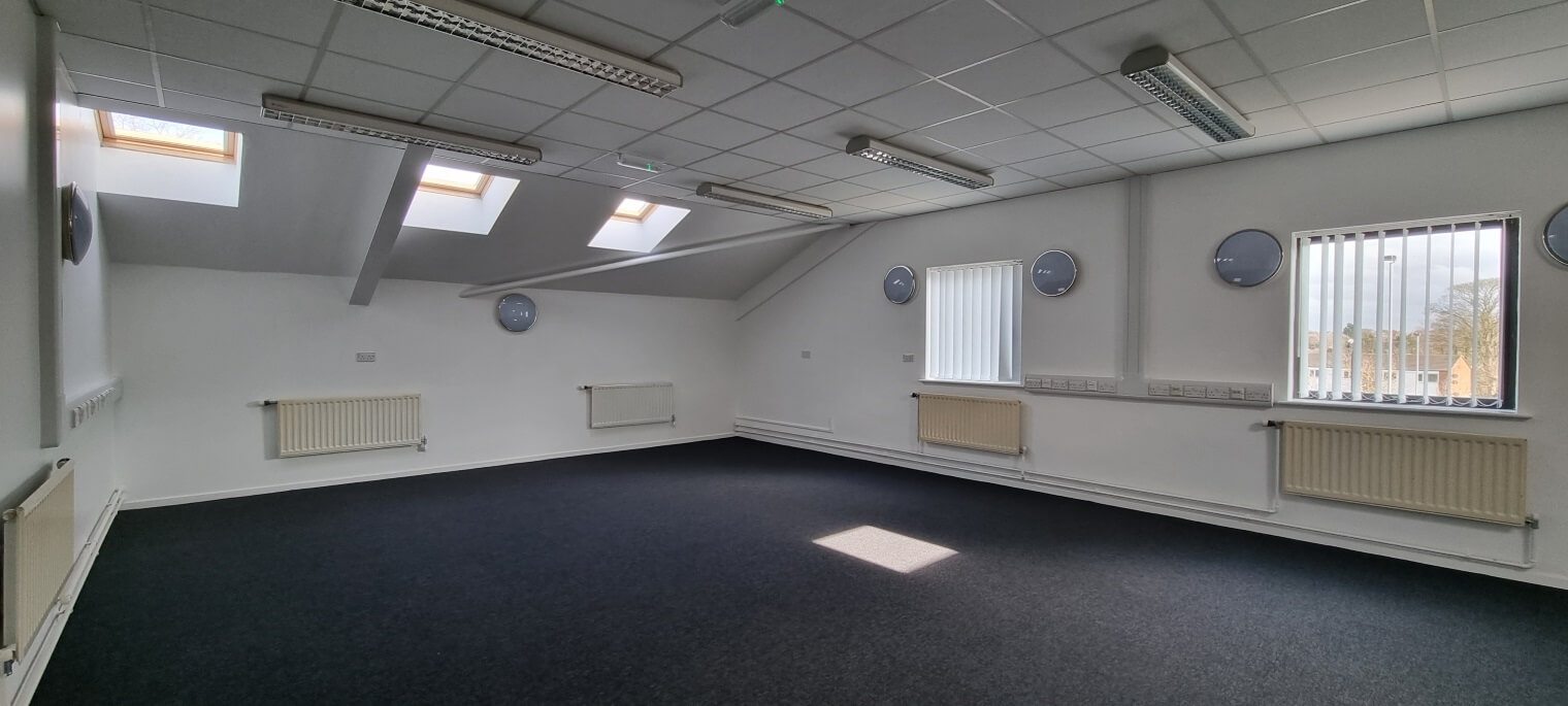 Large vacant room with a few windows and radiators