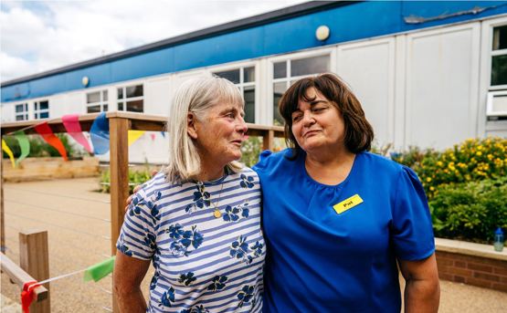 Two women smiling at each other in front of health centre with colourful bunting