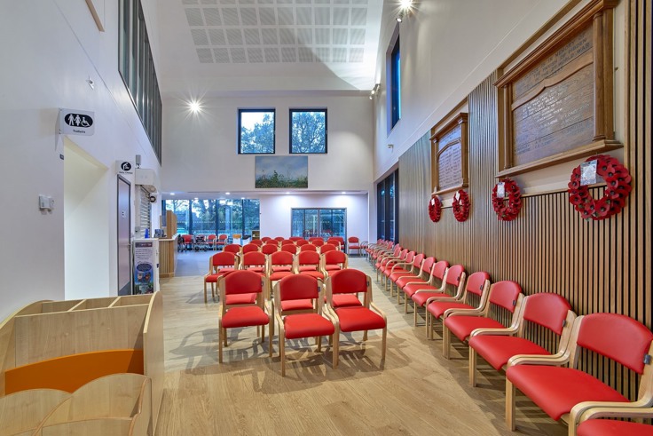 The interior of the new Hythe and Dibden War Memorial Hospital in the New Forest. There's a waiting room with seating in red colour and Remembrance Day poppy wreaths on the wall. There are floor to ceiling windows at the back of the room. 