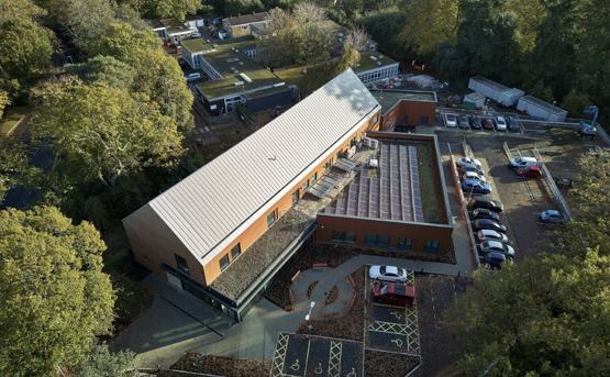 An aerial view of the exterior of the new Hythe and Dibden War Memorial Hospital. There's two parking areas and large trees. 