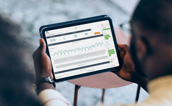 A person holding a tablet displaying a data analytics dashboard with charts, graphs, and performance metrics in a modern indoor setting.