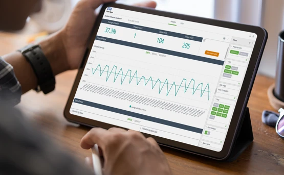 Person holding a tablet displaying a data analytics dashboard with graphs, percentages, and key metrics, including a line chart and various buttons and tabs on the screen.