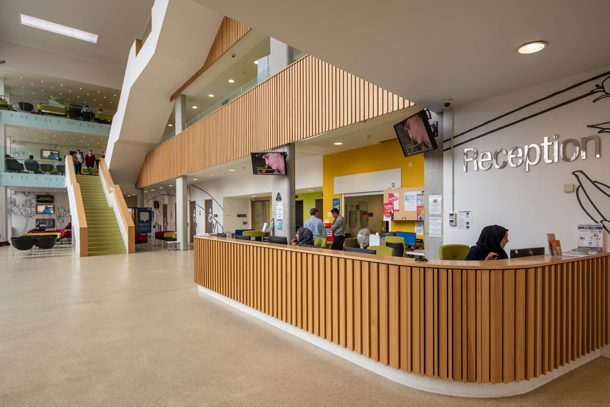 Reception area at a NHS site. The countertop is curved and has wooden panels. There's a 'Reception' sign above the space with the countertop and desks