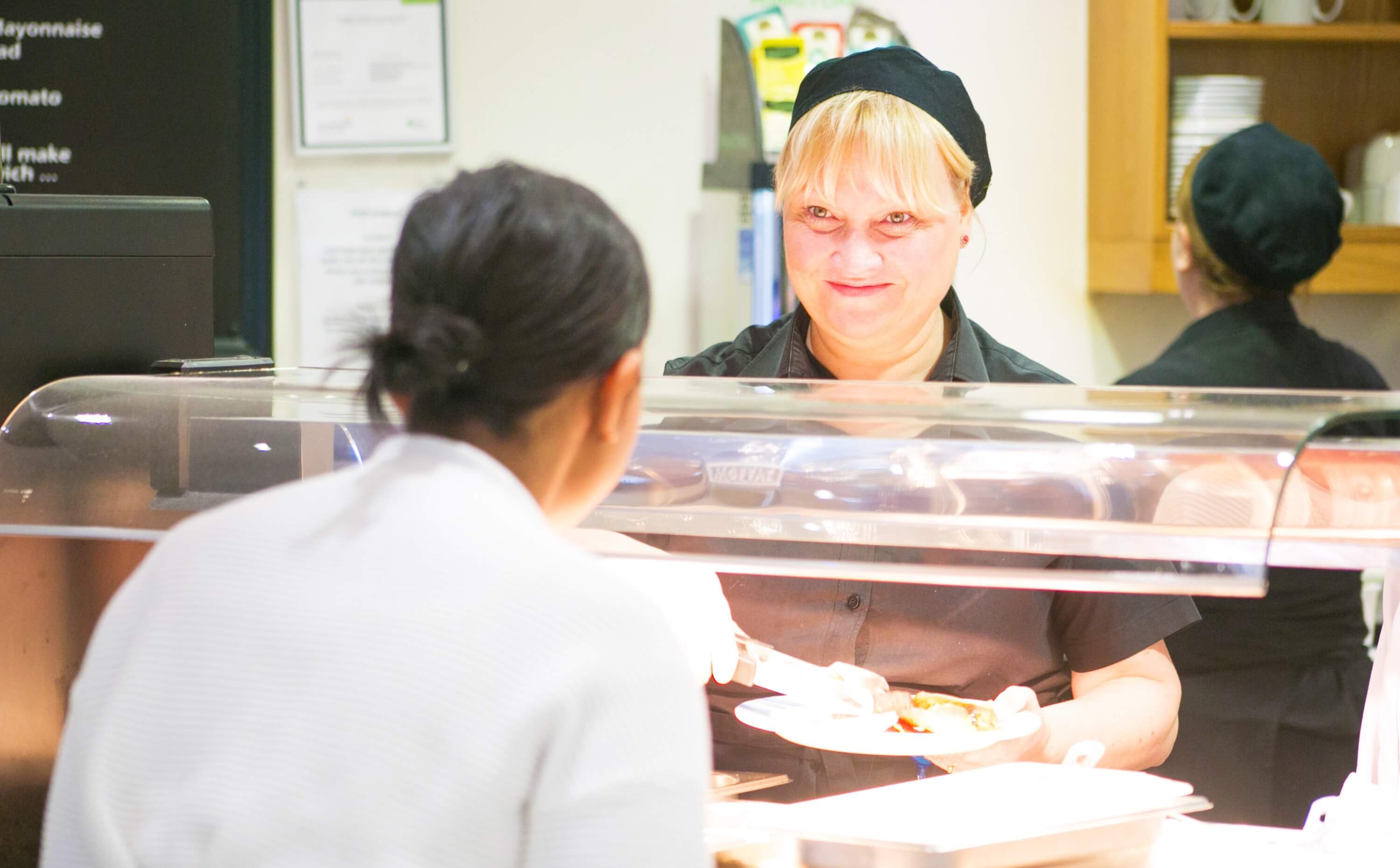 A female staff member serving food in a cafeteria
