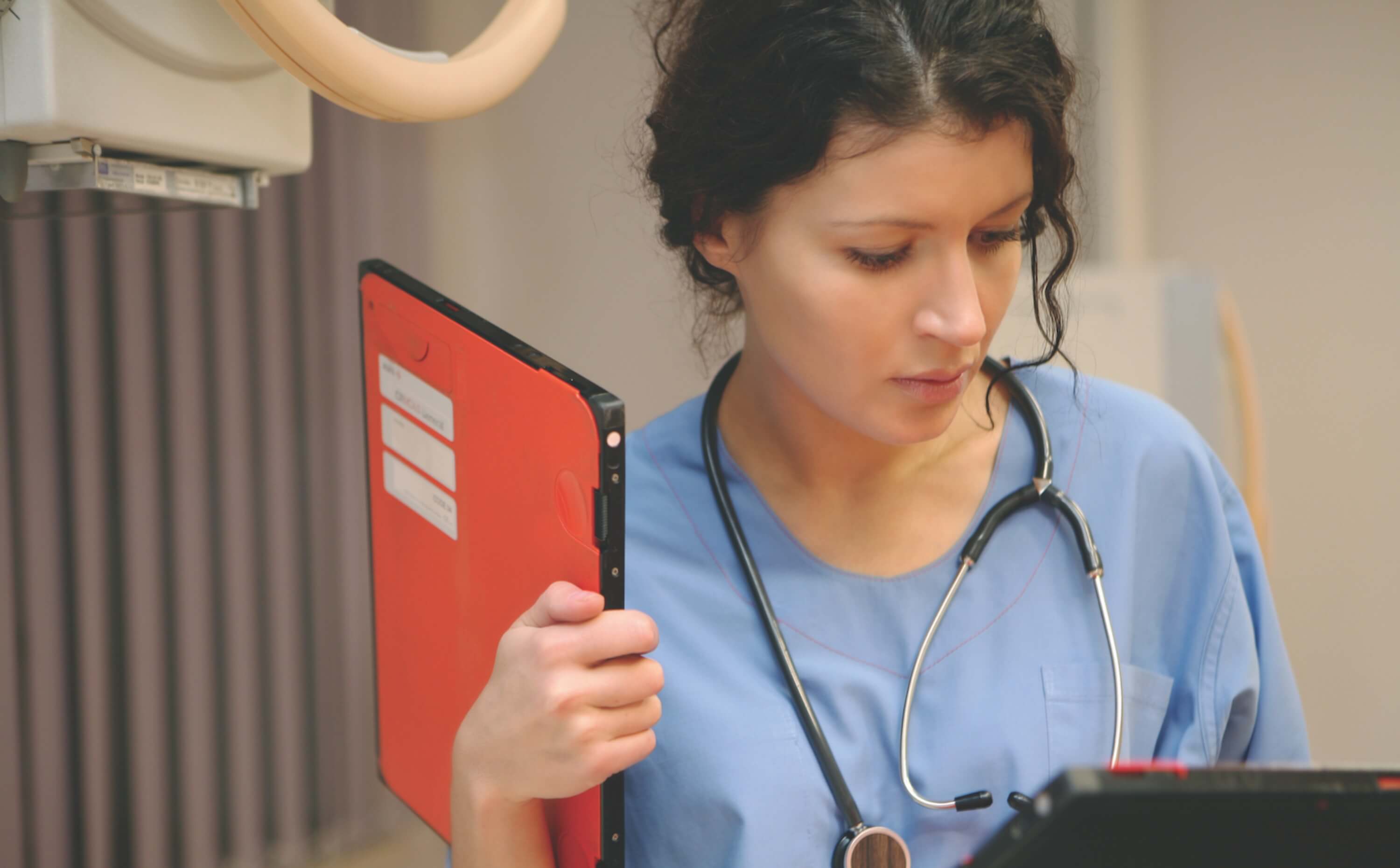 A female nurse entering information on a screen. She is holding a red file