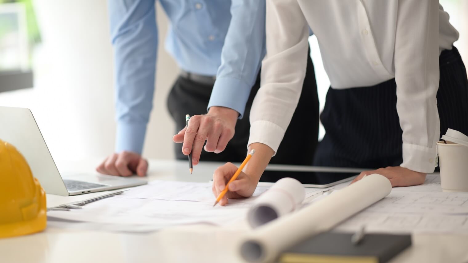 two people leaning over a desk looking at building plans