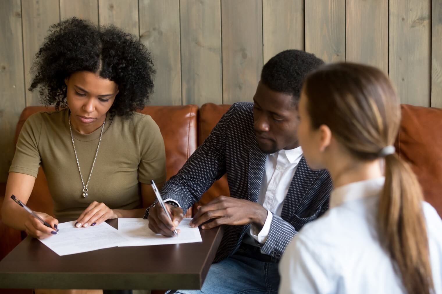 a couple signing paper on a table in front of a professional 