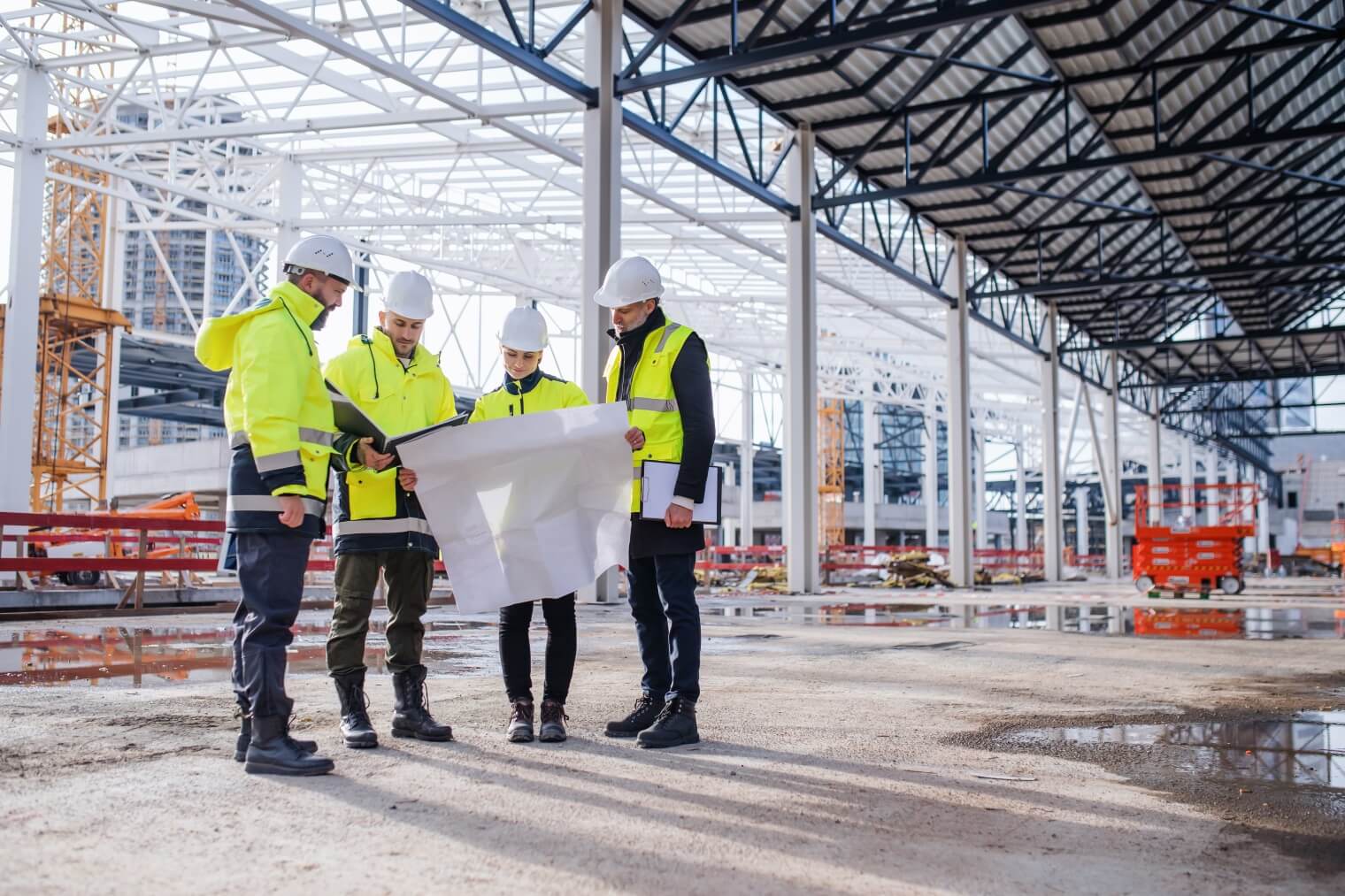 four construction workers in high-vis look at a large building plan