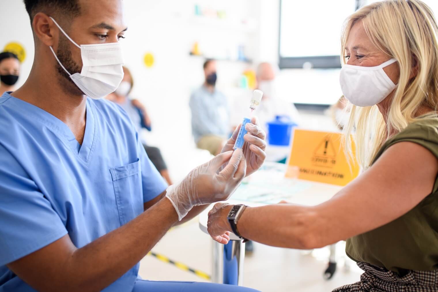 Woman with facemask getting vaccinated by male nurse 